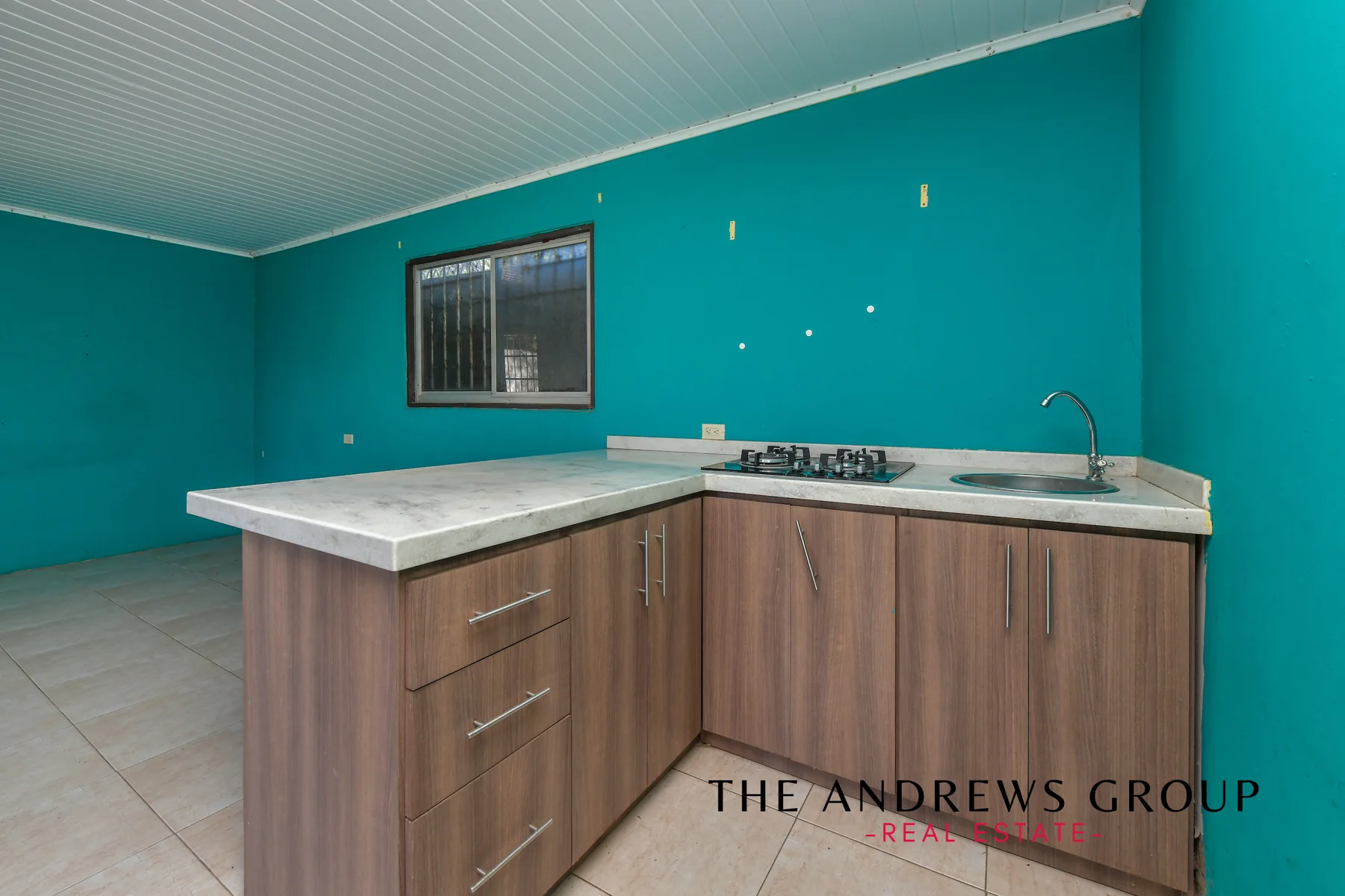 The apartment kitchen: teal walls, a peninsula unit in wood with a stone counter, gas hob and stainless sink, tiled floor.