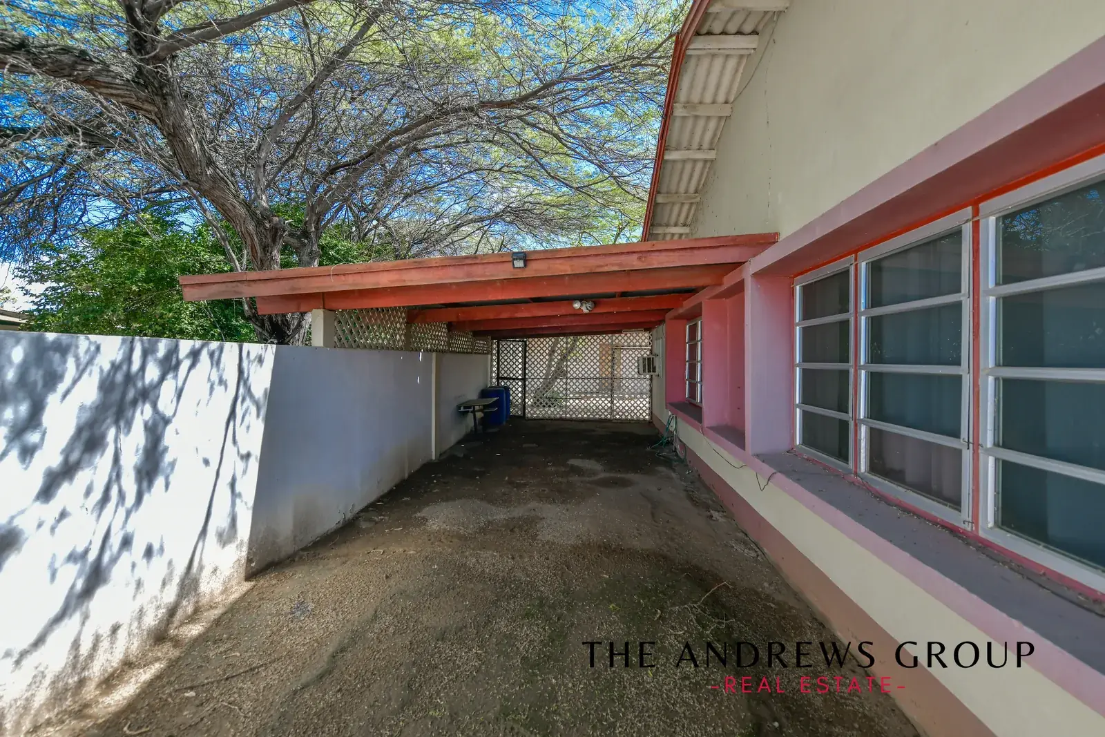 The covered carport running down the side of the house, with a lattice gate at the end and a mature tree overhead.