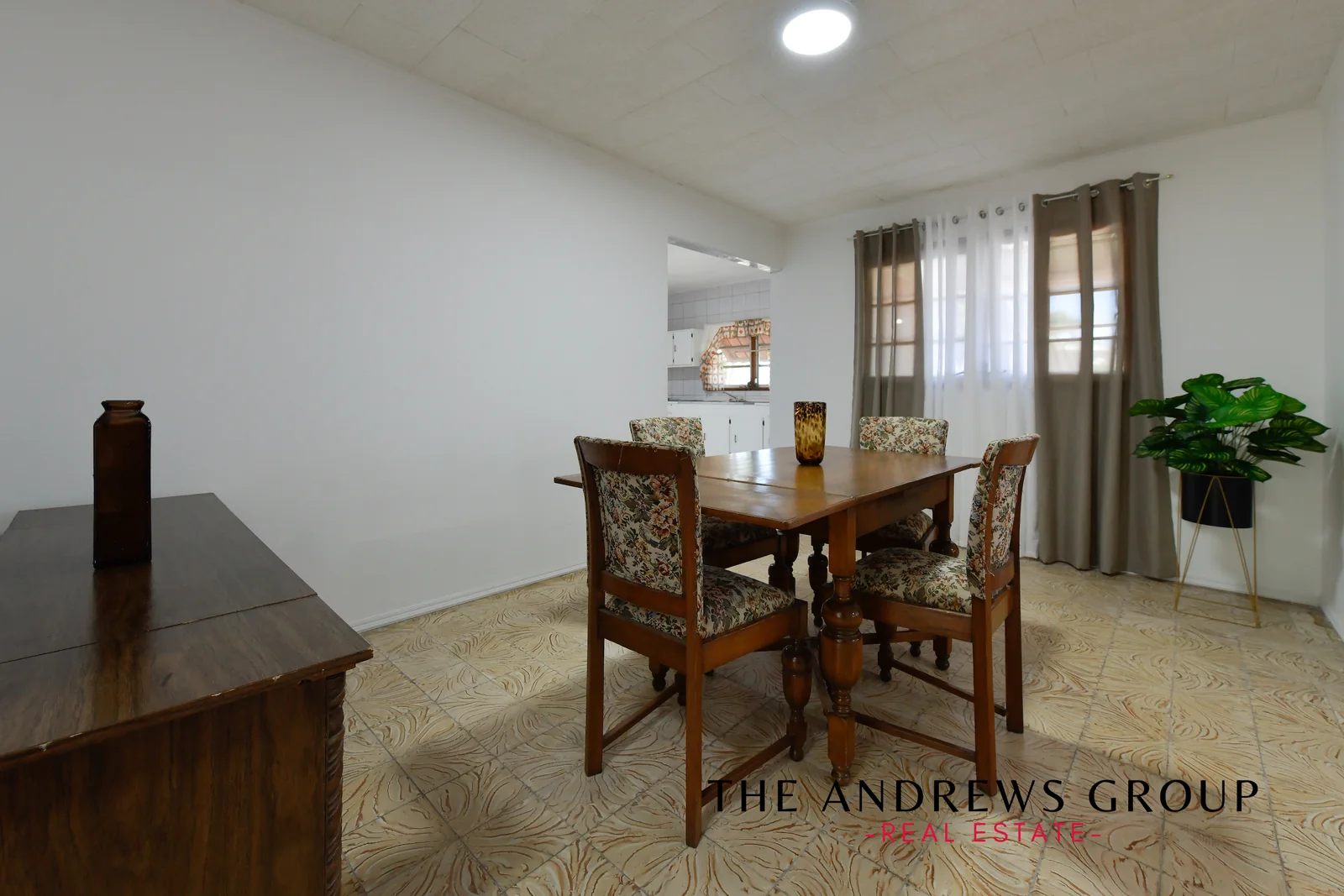 The dining room: patterned cream tile floor, white walls, a wooden table and chairs, the kitchen through the opening.
