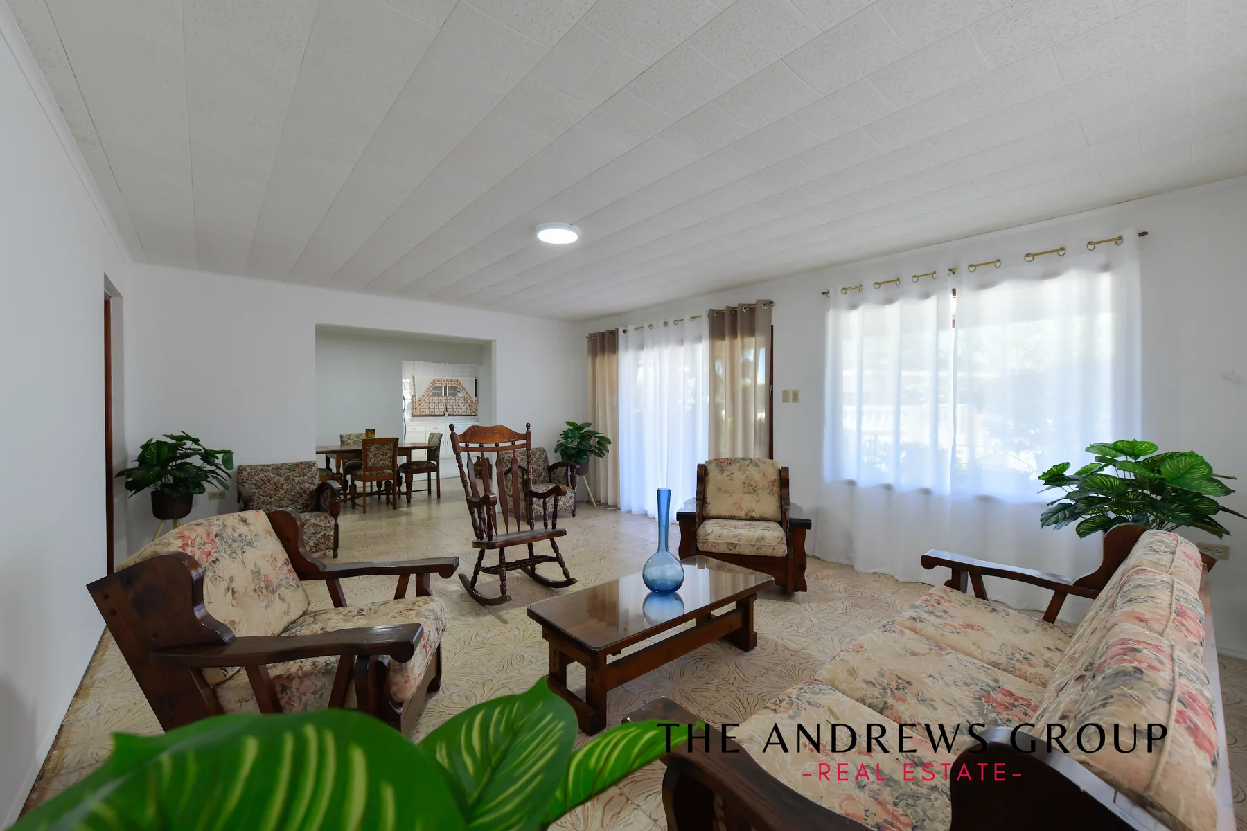 The main house living room: patterned tile floor, white walls, wooden furniture, opening through to the dining room and kitchen beyond.