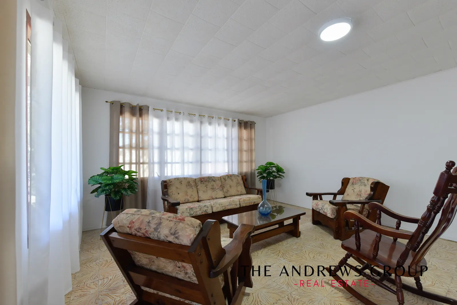 The living room: patterned tile floor, white walls, wooden furniture and plants, with light from two sides.