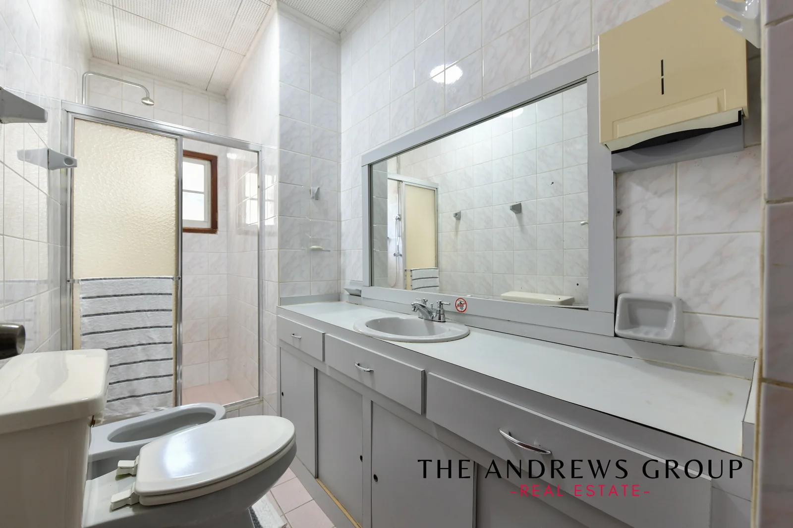 The master bathroom: white and pink marbled tile, a glazed shower enclosure, a bidet, and a long vanity under a full-width mirror.