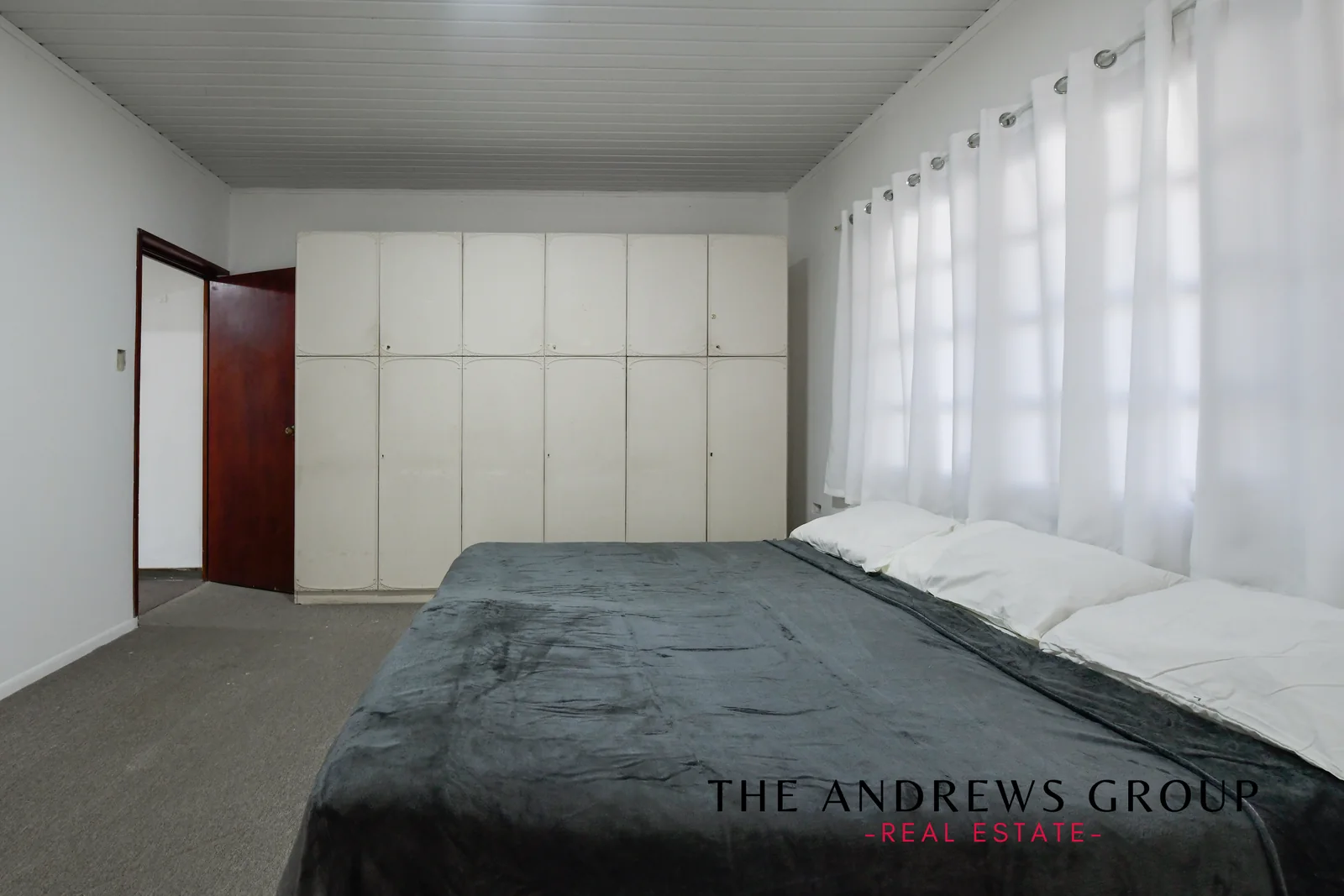 The master bedroom: grey carpet, white panelled doors along one wall, and a window running the length of another.