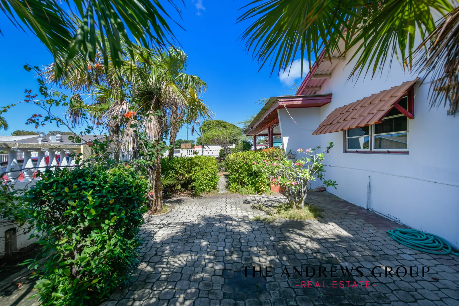The paved side yard: interlocking pavers, fan palms, frangipani in flower, and the tiled window awnings along the side of the house.