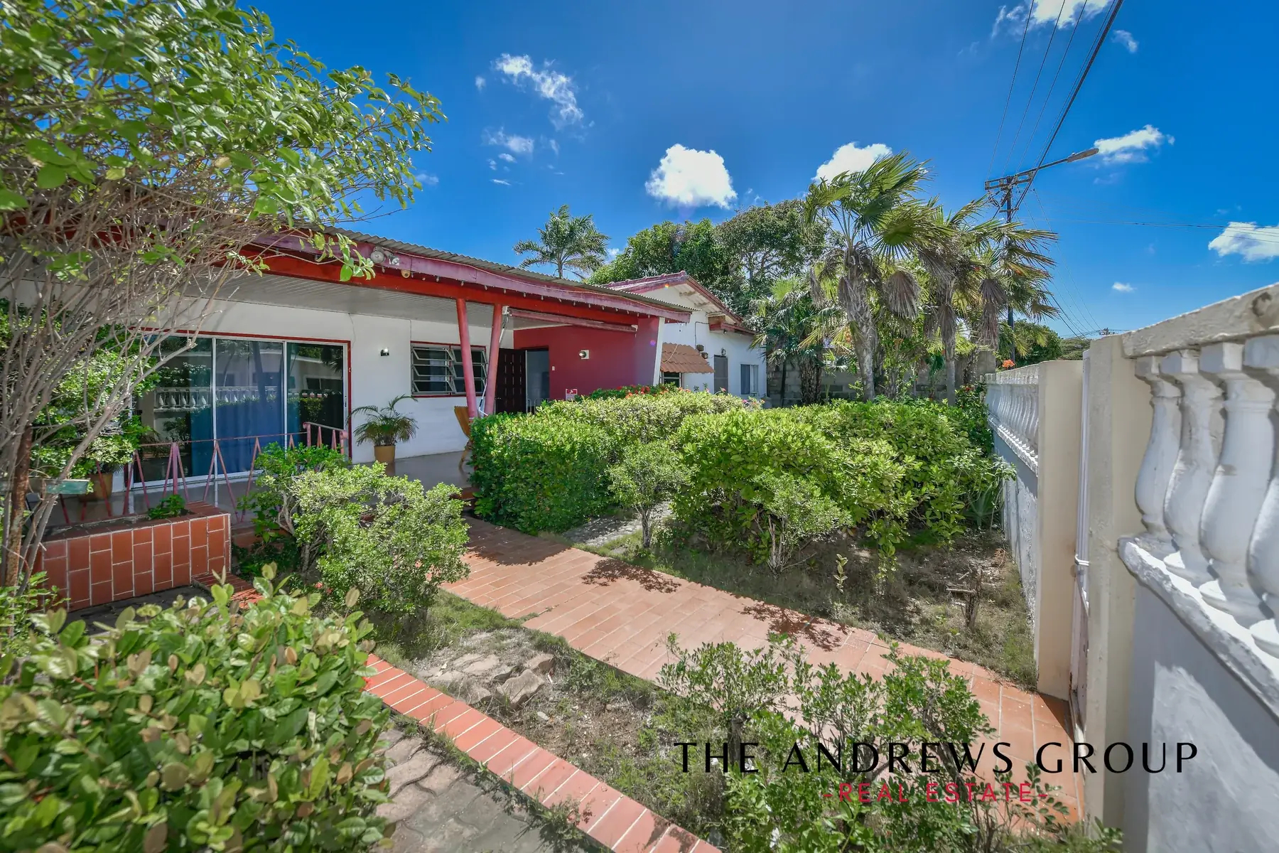The garden side of the house: hedges, a brick path, palms, and the red-posted veranda running along the front.